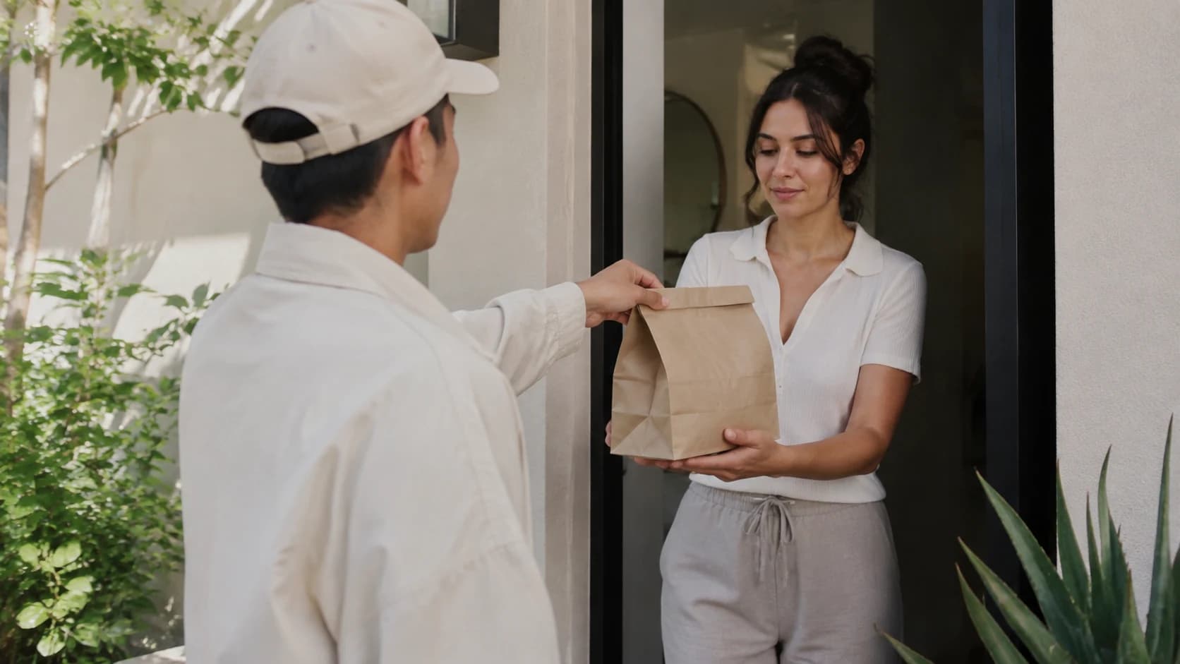 A courier handing a prepared meal order to the customer at their door